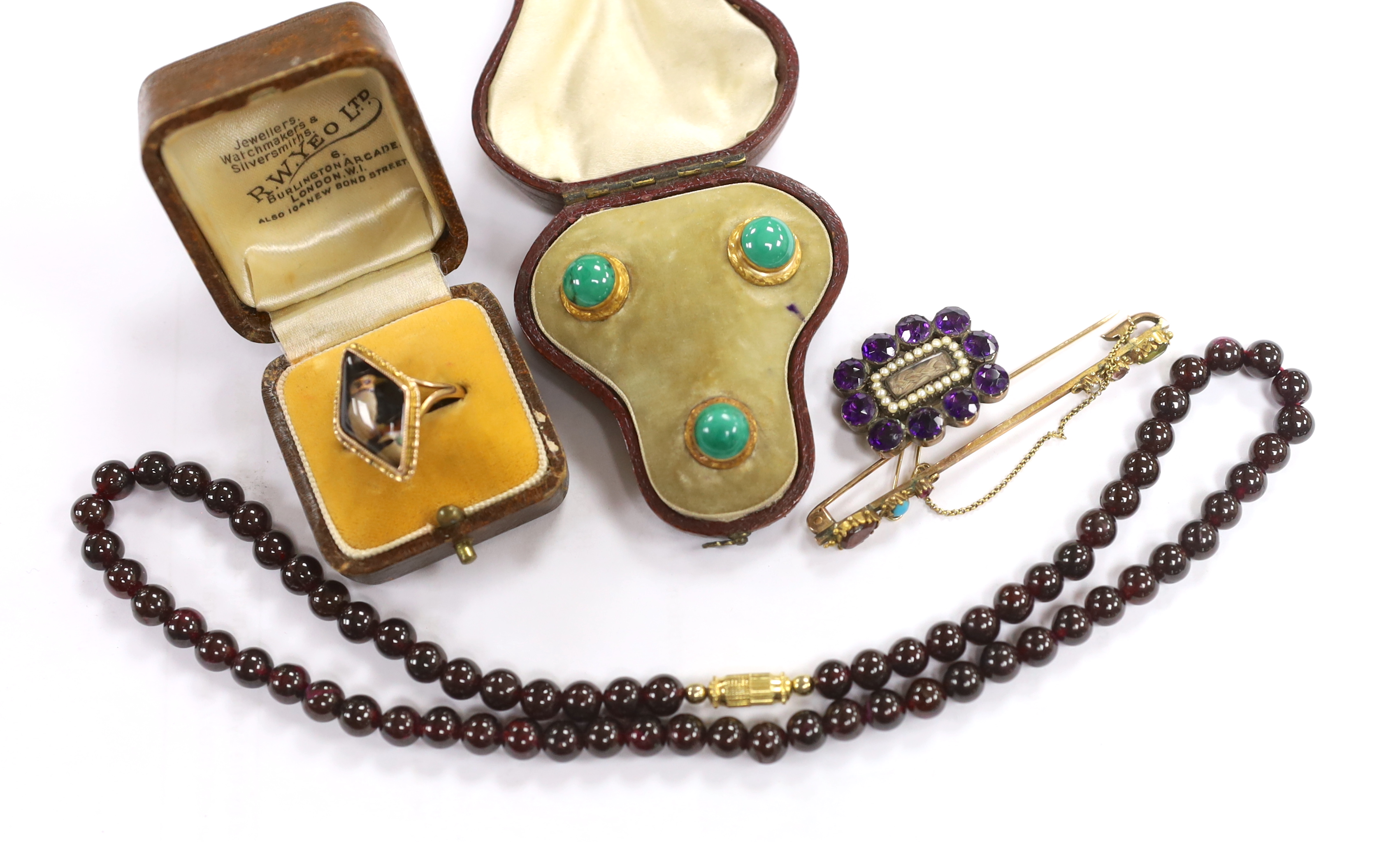 A Georgian amethyst paste and seed pearl set mourning brooch, with plaited hair, 27mm, a cased set of three Edwardian yellow metal and malachite set dress studs, a garnet bead necklace, brooch and a ring.